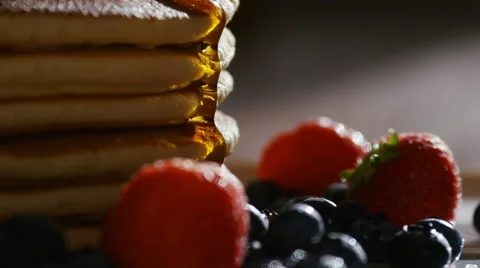Camera follows maple syrup being poured over hot stacked pancakes and fruit Stock Footage 65282150