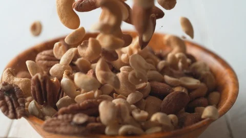 Camera follows peanuts, pecans and cashew nuts falling into a bowl. Slow Motion. Video stock 89809133