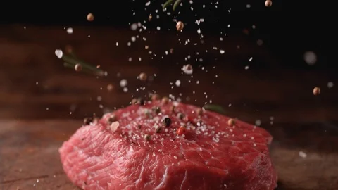 Camera follows putting herbs and spices on raw steak meat. Slow Motion. Stock Footage