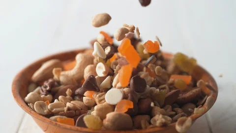Camera follows trail mix nuts and dried fruits falling into a bowl. Slow Motion. Stock Footage 89878576