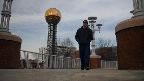 Camera follows a young man walking though World's Fair Park in Knoxville, Vídeos de archivo 101563670