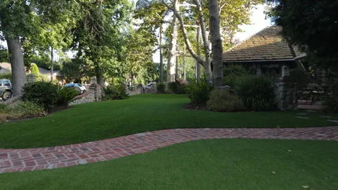Camera glides across a front lawn past a stone cottage and trees Stock Footage 345548606