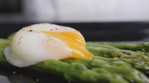 Camera glides past a poached egg with golden yolk flowing over green asparagus 库存影片 348688029