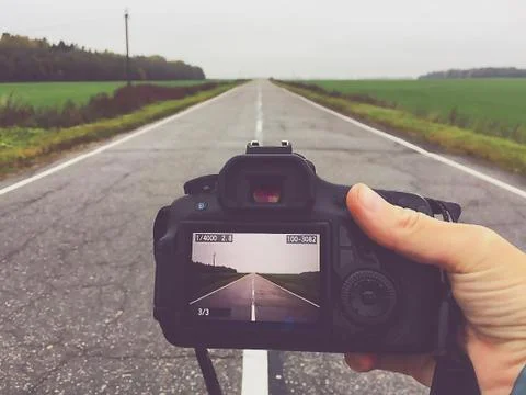 Camera in hand with the image of the road going into the distance Stock Photos