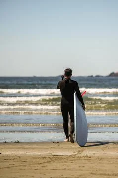 Camera in hand taking a video of himself walking in the ocean water to surf the Stock Photos