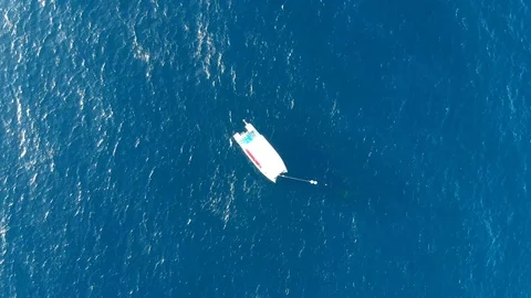 Camera hangs over blue open calm ocean and white boat Stock Footage 101484974