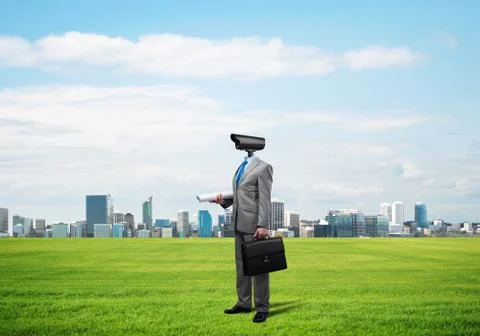 Camera headed man standing on green grass against modern cityscape Stock Photos