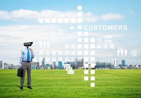 Camera headed man standing on green grass against modern cityscape Stock Photos
