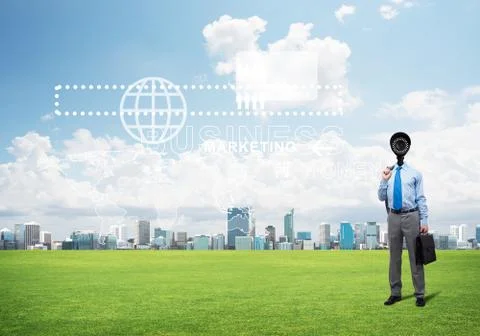Camera headed man standing on green grass against modern cityscape Stock Photos