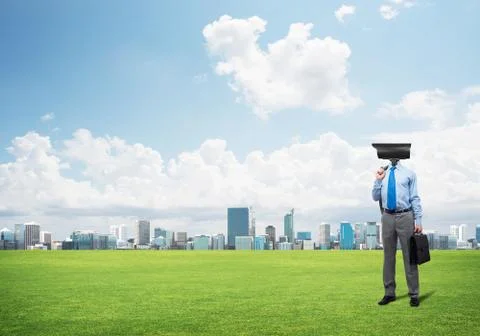 Camera headed man standing on green grass against modern cityscape Stock Photos