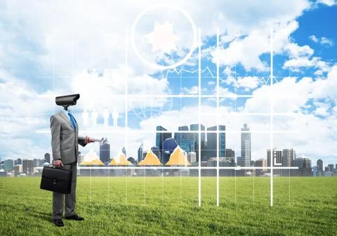 Camera headed man standing on green grass against modern cityscape Stock Photos
