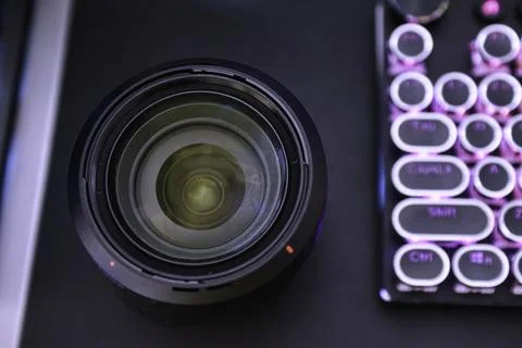 Camera lens on a dark surface next to a colorful mechanical keyboard with round Stock Photos