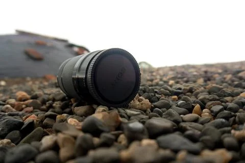 Camera Lens Left Behind on Pebble-Covered Surface - Photography Equipment. 스톡 사진