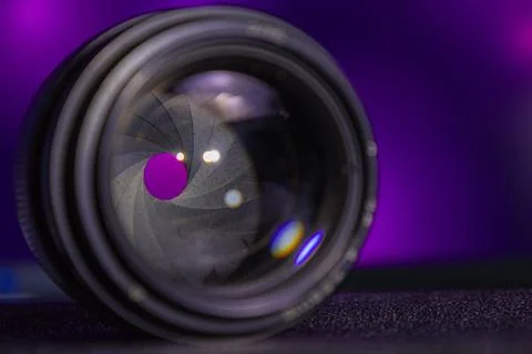 Camera lens rests on a table with a purple background and light reflected in the Stock Photos
