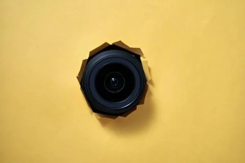 A camera lens is shown through a hole in a yellow background Stock Photos