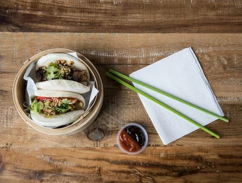 Camera looks down on wooden table with two bao buns Stock Photos