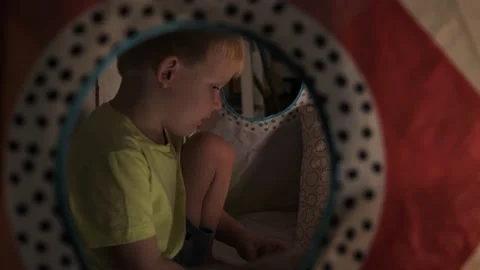 The camera looks at the little boy through the window in the tent at home Stock Footage 235544466