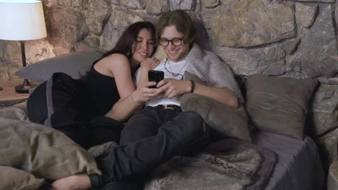 Camera In Motion A Young Couple Are Lying In Bed Chatting Looking At Photos Stock Footage 137732319