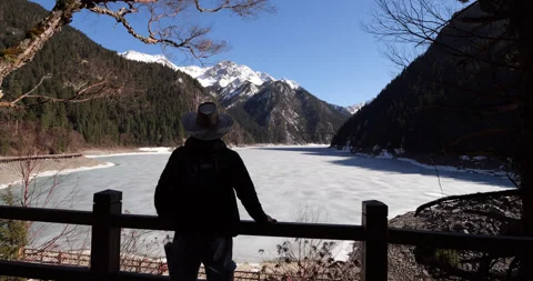 Camera move backwards, reveal standing man looking at frozen Long Lake Stock Footage 321234154