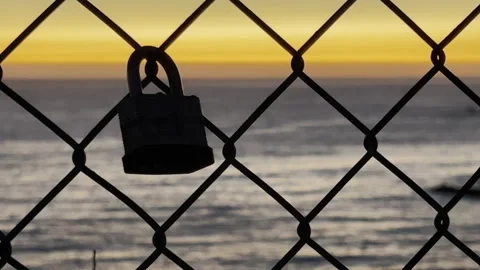 Camera movement accentuates this lone padlock in silhouette on a chainlink fence Stock Footage 164563900