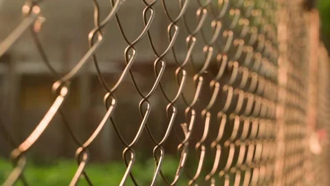 Camera movement along the chain-link fence illuminated by the morning dawn sun Stock Footage 203837729