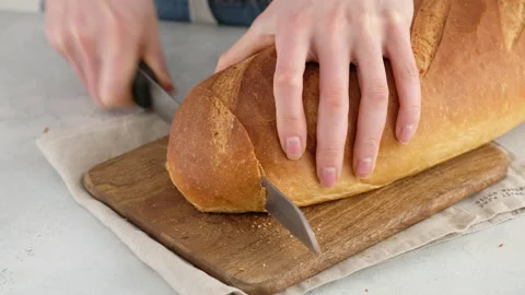 Camera movement. Close-up of female hands cut hot wheat bread on a wooden board Stock Footage 146142076