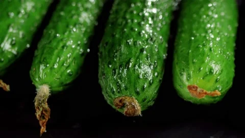 Camera moves up above fresh green juicy cucumbers on black board on wooden table Stock Footage 130515930