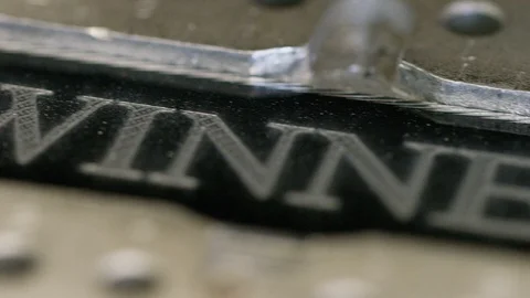 Camera moves across a CNC engraved surface with the etched word WINNER 库存影片 102285383