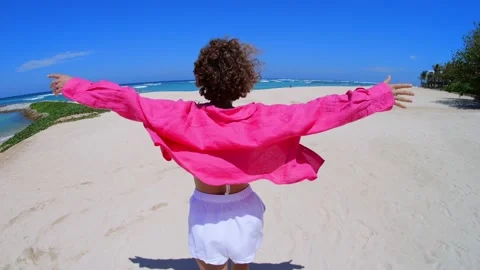The camera moves after the curly-haired woman walking along the sea beach and Stock Footage 220397594