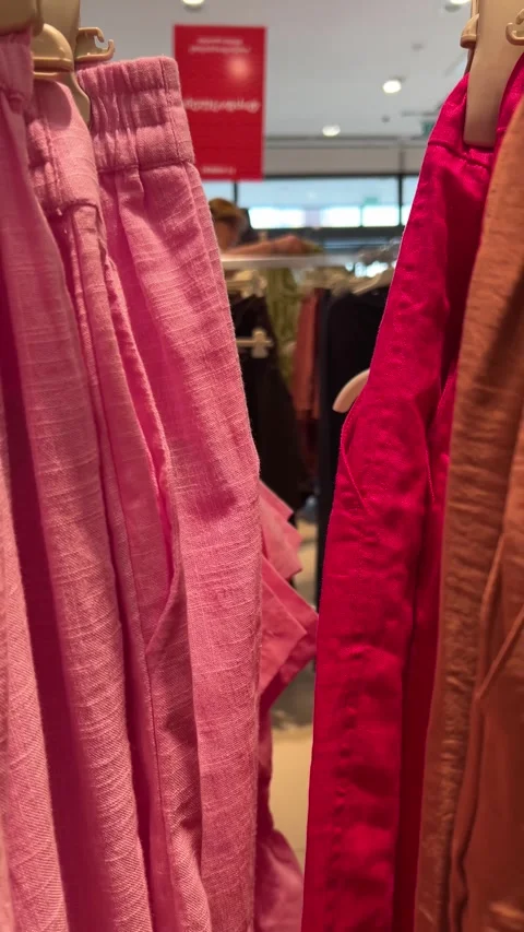 Camera moves along shelf with clothes on hangers, pink magenta cotton pants Stock Footage 314828572