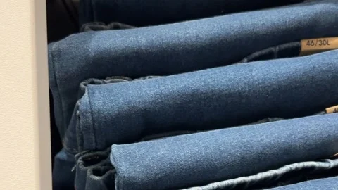 Camera moves along shelf with new blue jeans pants, denim clothes Stock Footage 332574271