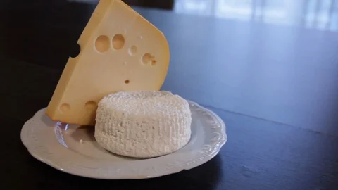 The camera moves around the plate on the table with Emmental and Adygei cheese. Video stock 112538176