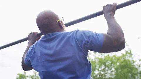 Camera moves around a senior man doing pull ups on a fitness bar in an outdoor g Stock Footage 195125700