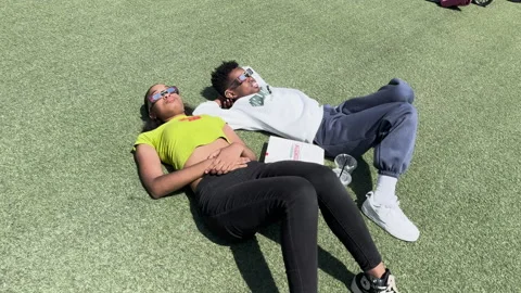 Camera moves around teens lying on ground watching solar eclipse Stock Footage 271599063