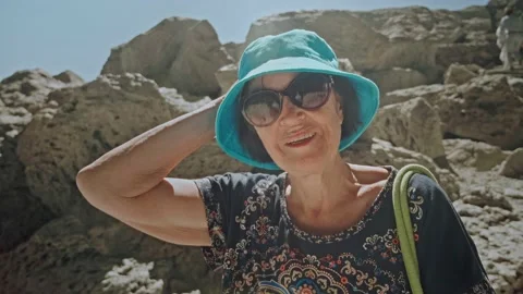 Camera moves away from pretty elderly woman standing on mountain hiking trail Stock Footage 222678406