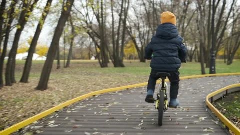 Camera moves behind little boy on children bike, riding along path in city park. Stock Footage 171413485