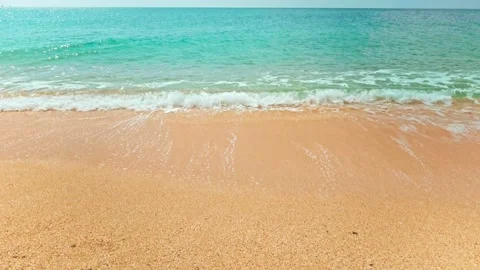 Camera moves down from clear blue sky to crystal clear sea washing sandy beach Stock Footage 190022056
