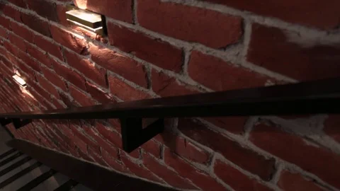 Camera moves down an empty staircase along a brick wall with lamps in the loft Stock Footage 111812145