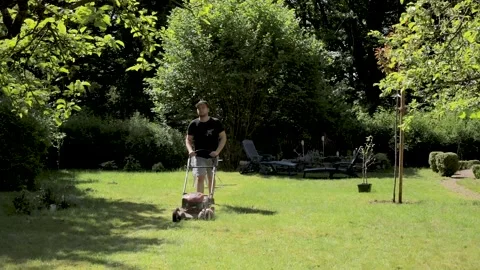 Camera moves down to a gardener mowing the grass in the backyard. Stock Footage 131611211