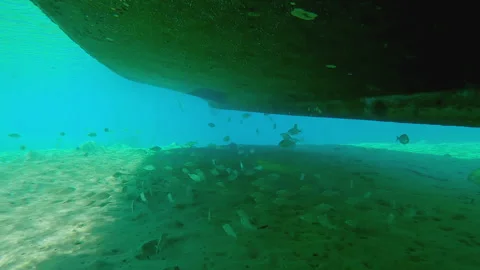 Camera moves forward under fishing boat moored above sandy seabed Stock Footage 332235519