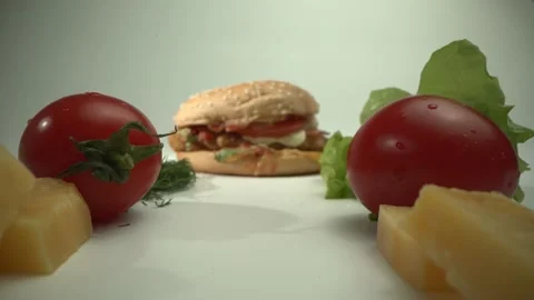 The camera moves past tomatoes, cheese and herbs to a delicious hamburger. Fresh Stock Footage 130558008