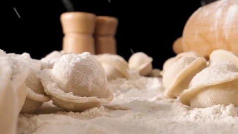 The camera moves slowly through the dumplings and flour. Flour is poured on top. Видео 144907173