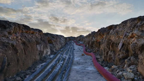 A camera moves through a dug trench lined with pipes and cables. Stock Footage 281651953