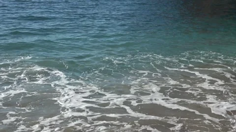 Camera moves from white pebbles and waves to a view of the sun shining over  스톡 동영상 332860929