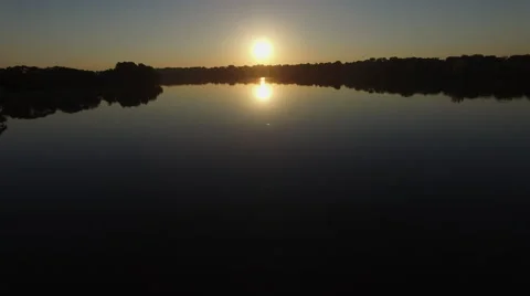 Camera moving above glassy calm water towards sunset Stock Footage 68653596