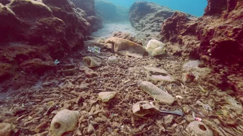 Camera moving back between two rocky reefs revealing view of massive plastic Stock Footage 288679470