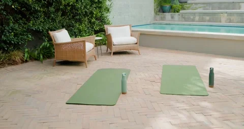Camera moving closer at poolside patio, framing green yoga mats with bottles to Stock-Footage 344331433