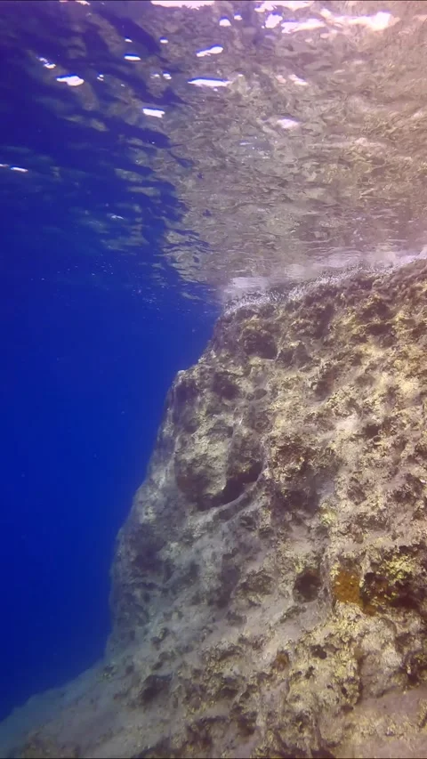 Camera moving forwards along cliff wall with reflected in surface, on blue water Stock Footage 255110609