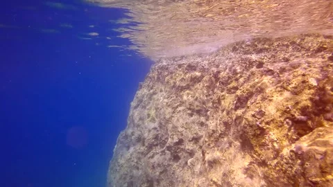 Camera moving forwards along cliff wall with reflected in surface, on blue water Stock Footage 255110728