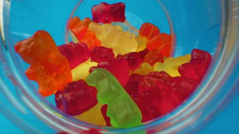 Camera moving out of sweet candy jar. Gummy bears in jar on blue background Stock Footage 139308125